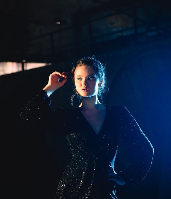 Woman performing a fluid, energetic movement in a dark studio with light blue highlights.